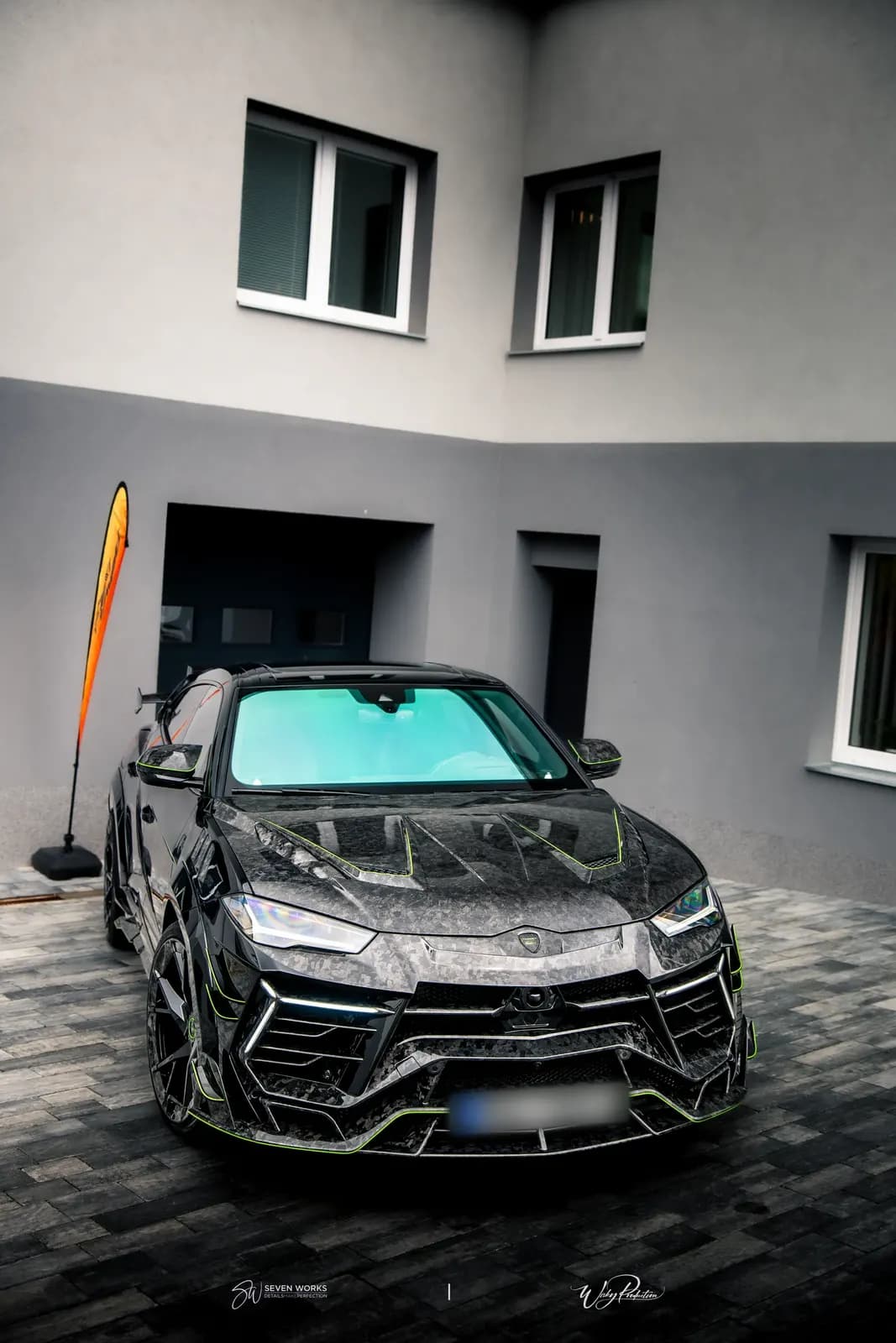 Lamborghini Urus s karbonovou kapotou a zelenými linkami zepředu před domem.