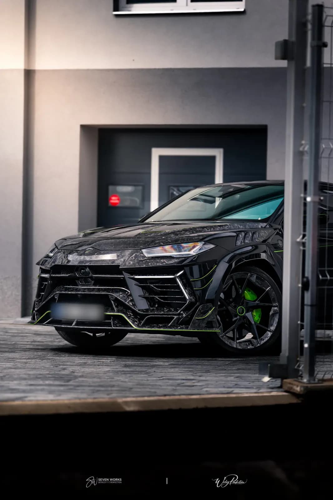 Lamborghini Urus zepředu-boku před garážovými vraty domu, zelené brzdové třmeny.