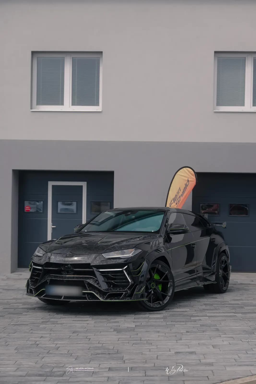Lamborghini Urus zepředu-boku na dlážděném nádvoří, v pozadí vlajkový banner FlexiShield.
