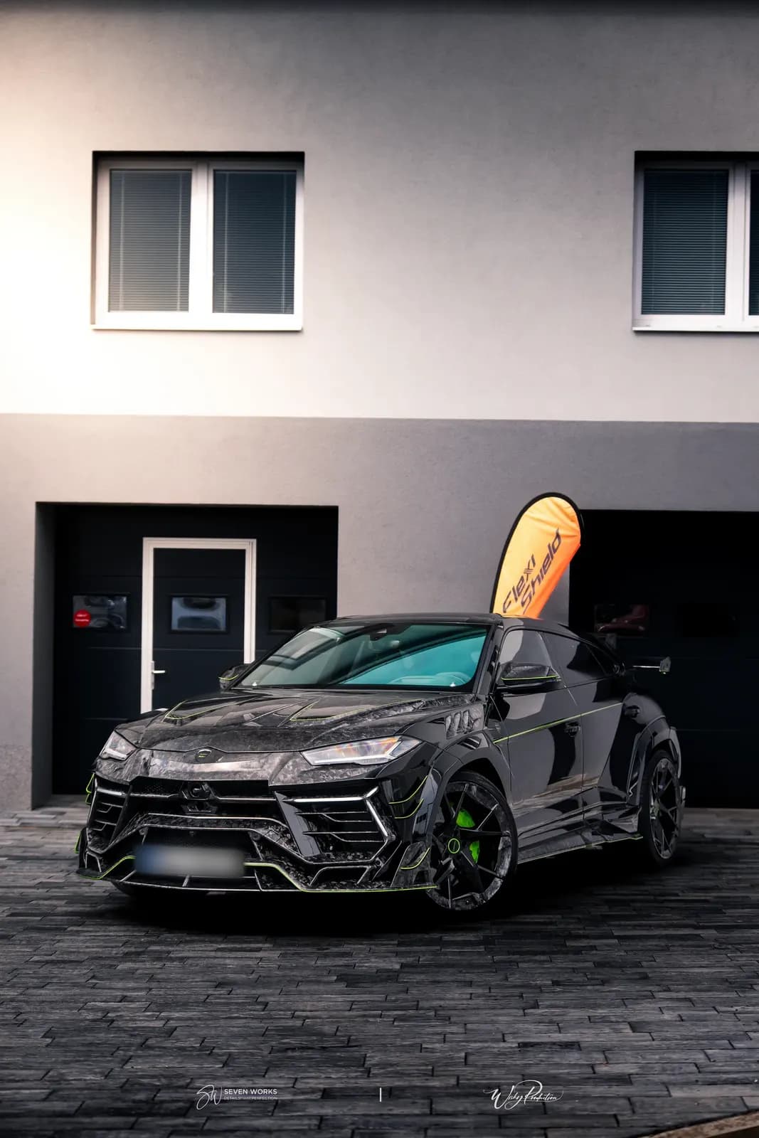Lamborghini Urus zepředu-boku v podvečerním světle před domem s garážemi.