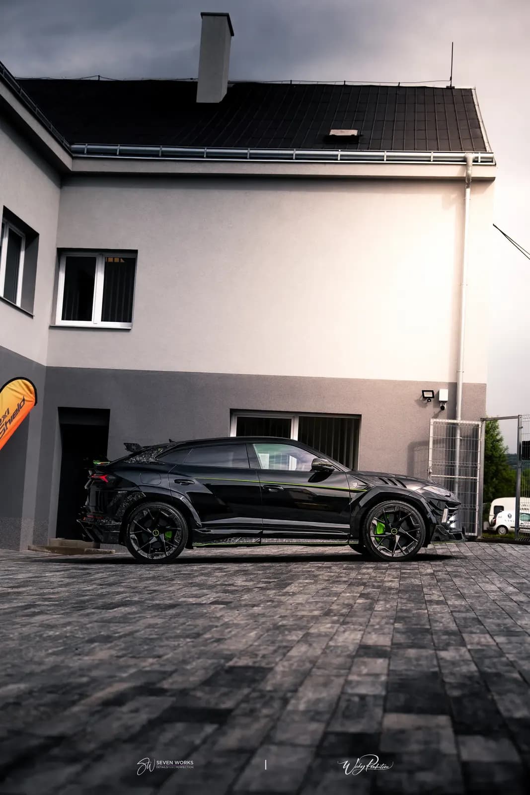 Boční siluetový pohled na Lamborghini Urus před domem pod dramatickou zamračenou oblohou.