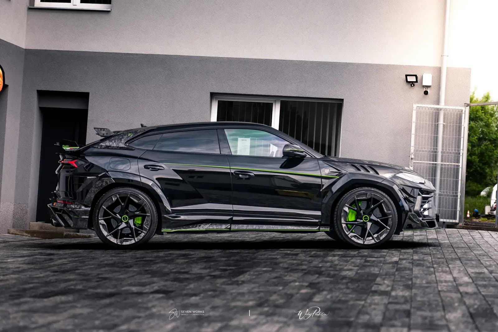 Boční profil Lamborghini Urus s karbonovým widebody kitem a zelenými linkami před domem.