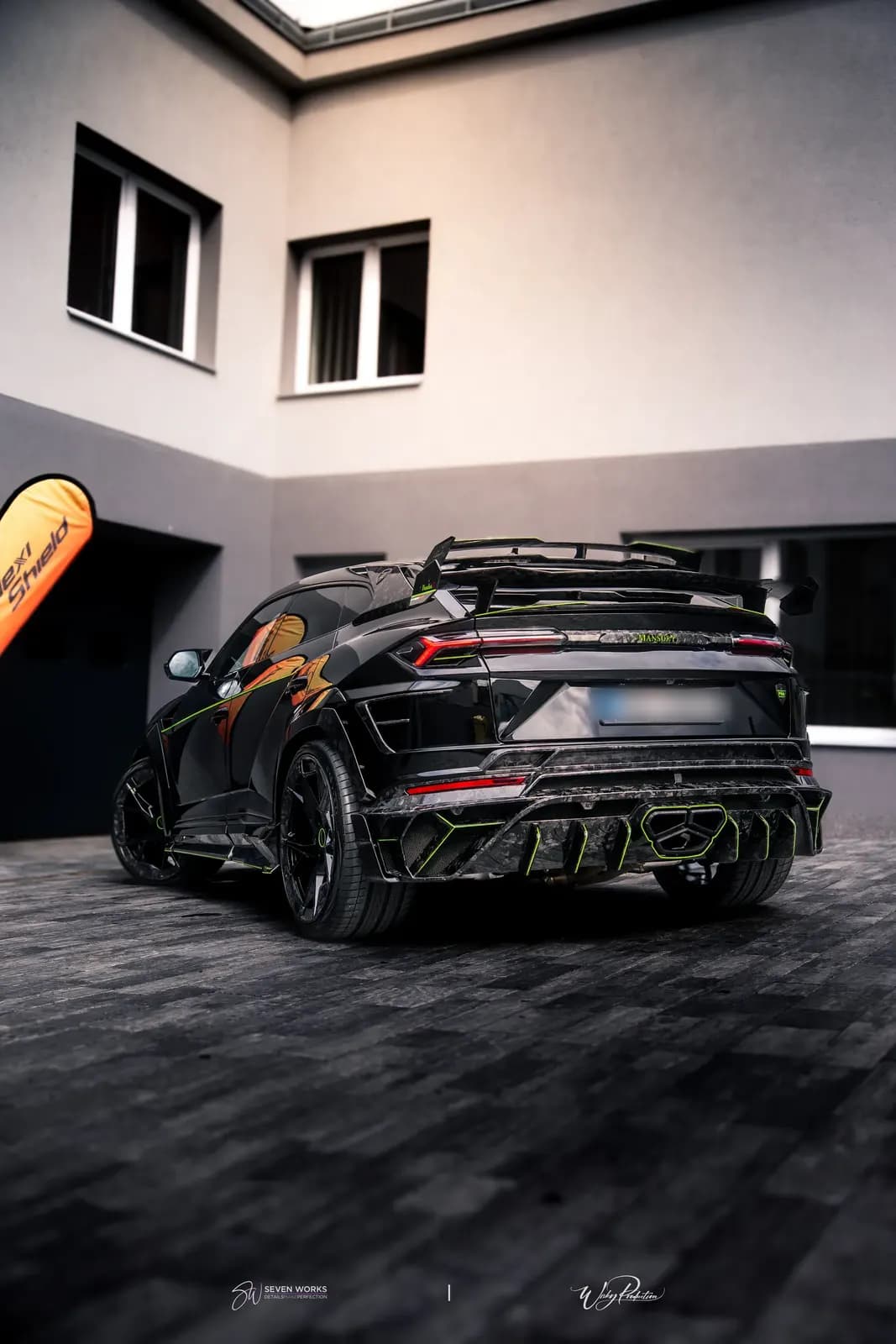 Lamborghini Urus zezadu-boku na dlážděném nádvoří s reklamní vlajkou FlexiShield.