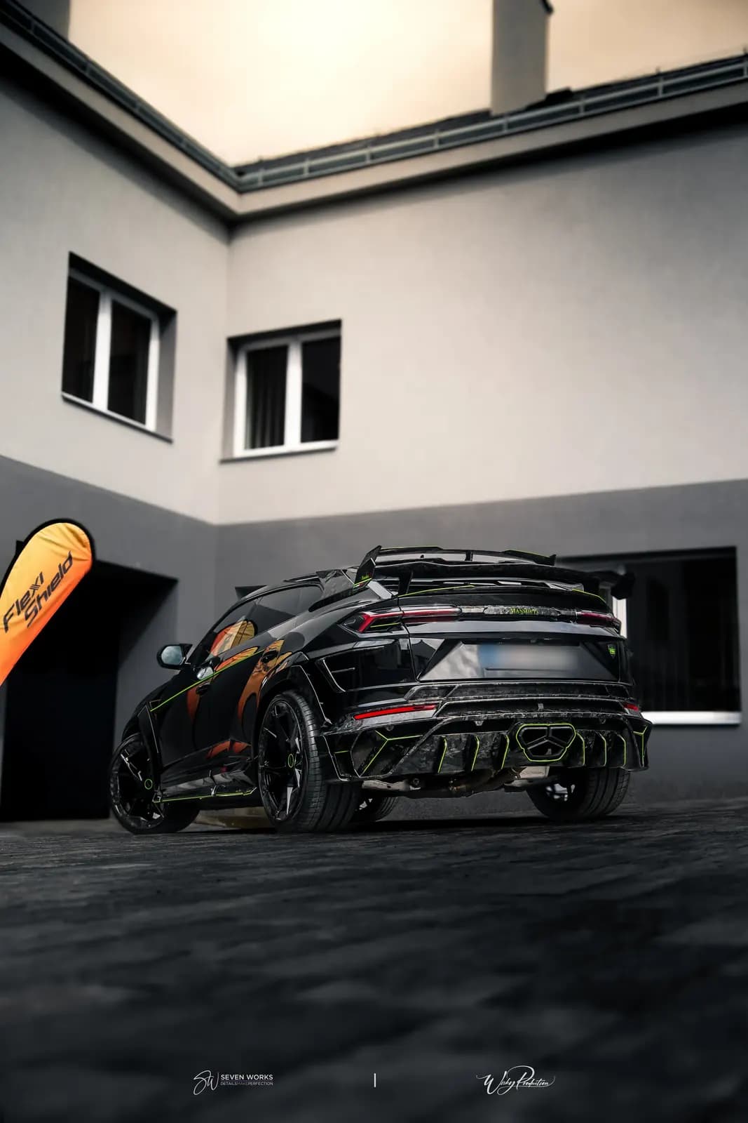 Lamborghini Urus zezadu zboku z nízkého úhlu na nádvoří před domem, vlevo vlajka FlexiShield.