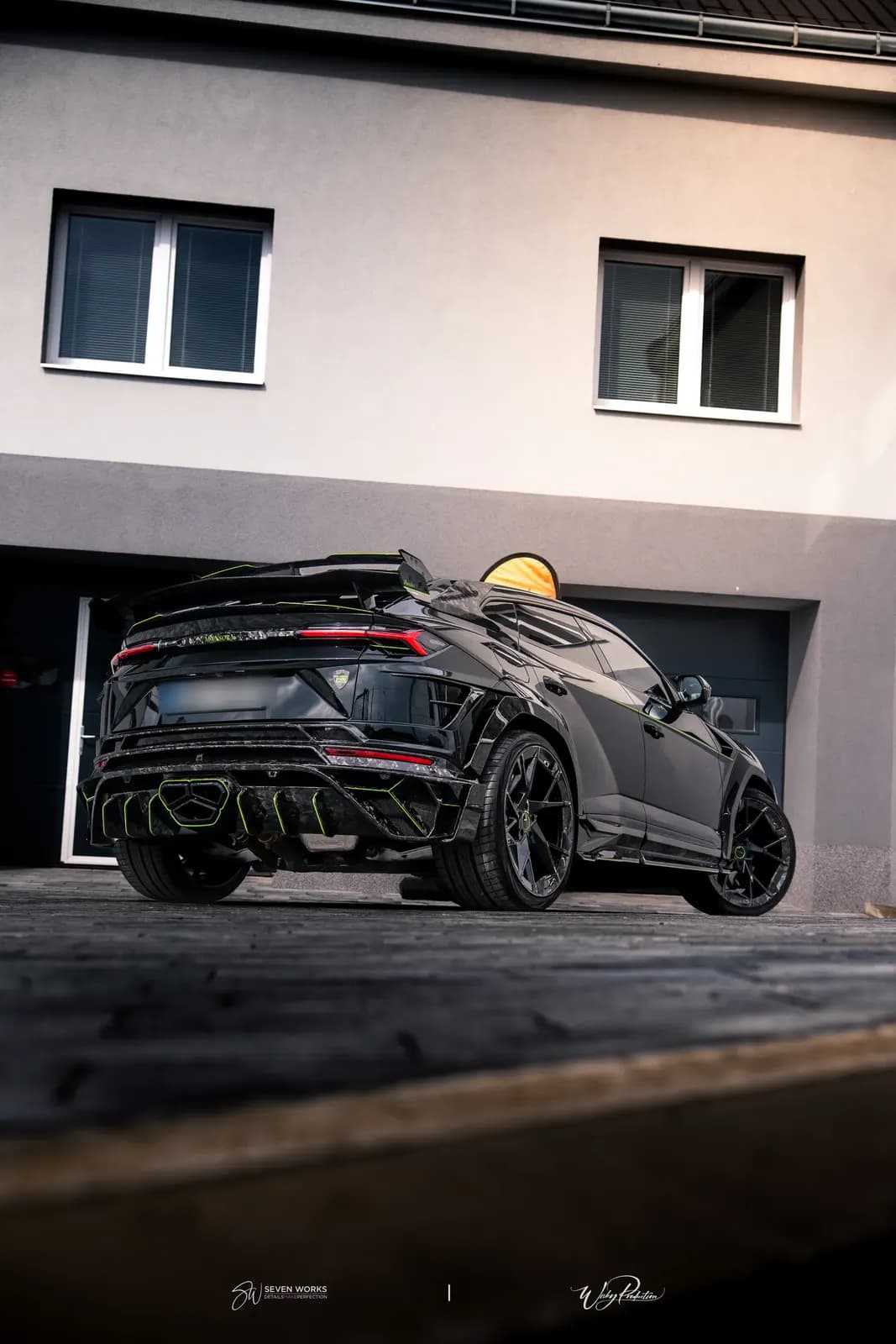 Lamborghini Urus zezadu-boku z nízkého úhlu před garážemi domu v podvečer.