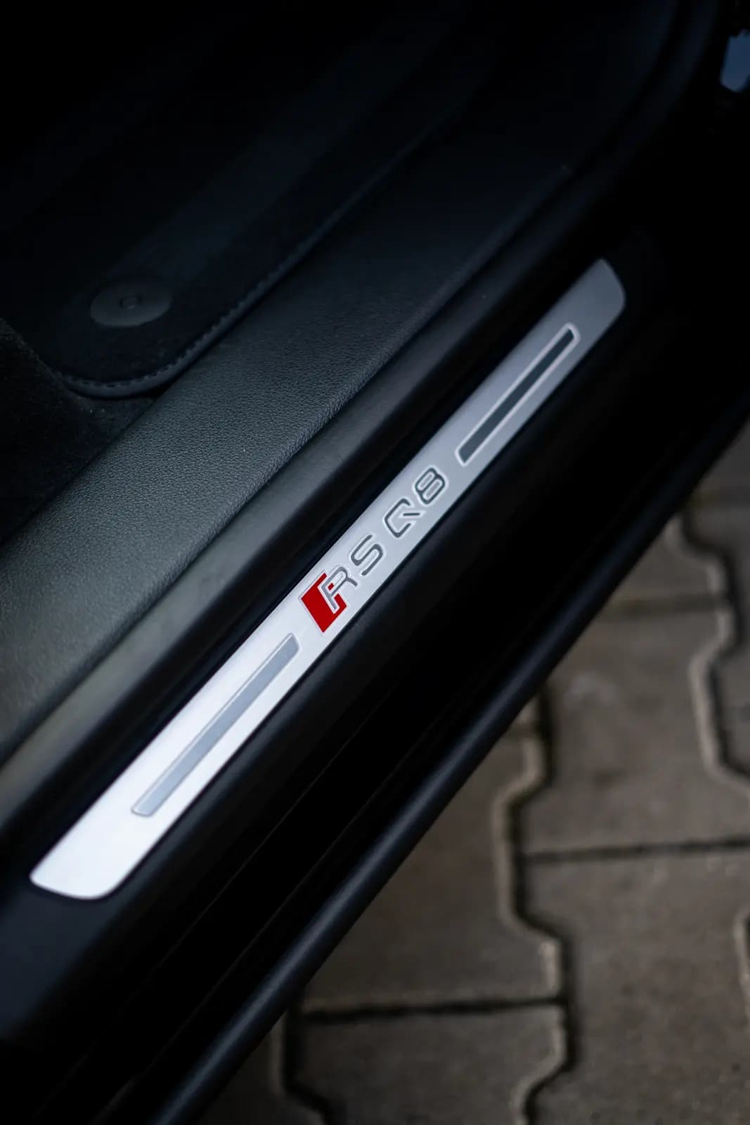 Door sill plate reading “RS Q8” with the Audi badge, the door open over paving.