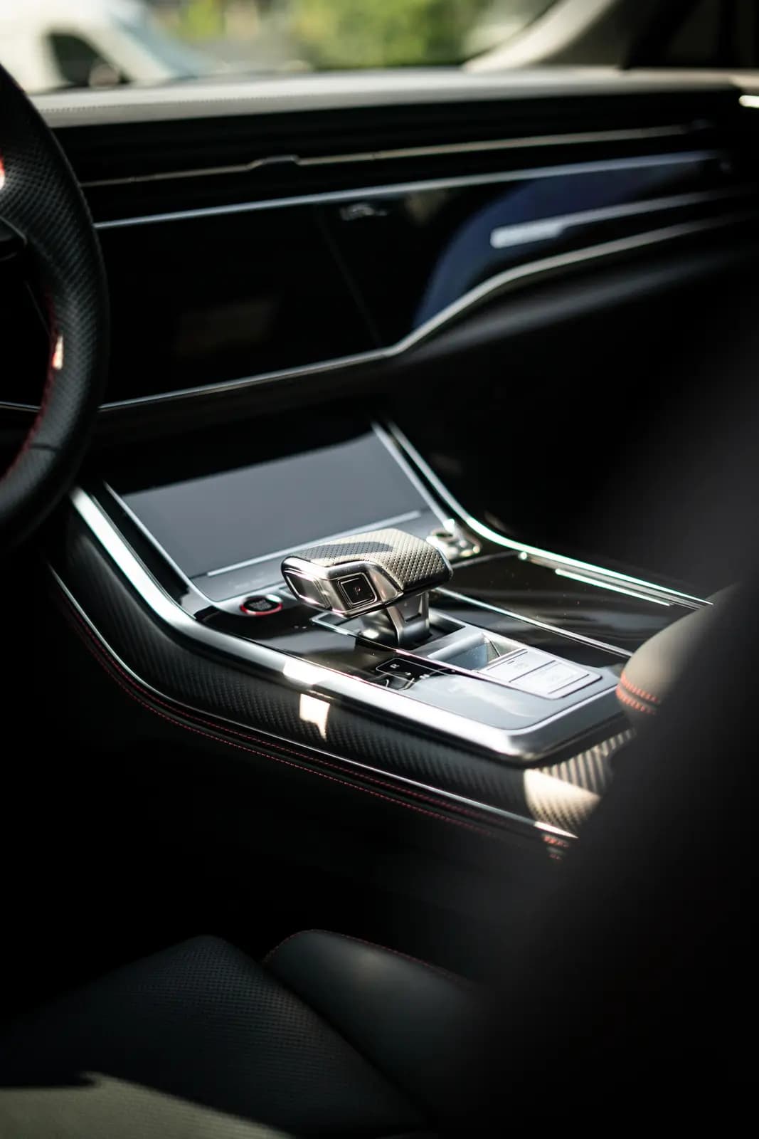 Gear lever and dashboard with carbon trim, greenery and a sunbeam blurred behind.