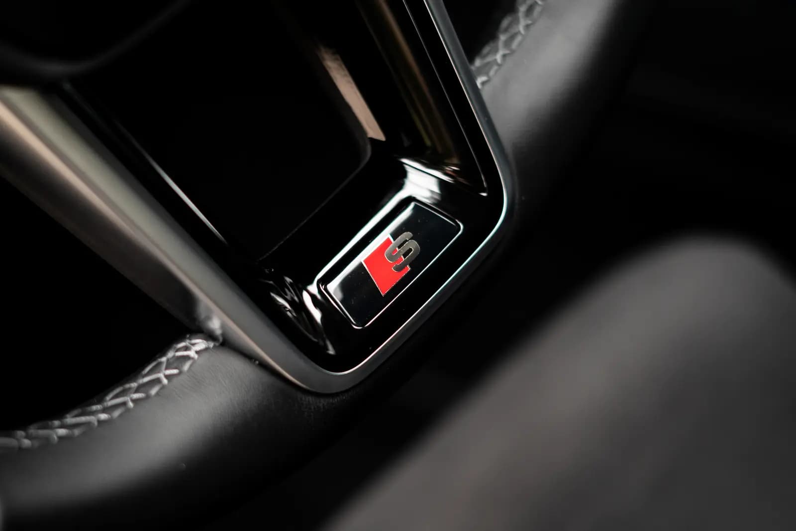 Red and chrome S badge on a black steering wheel with white stitching.