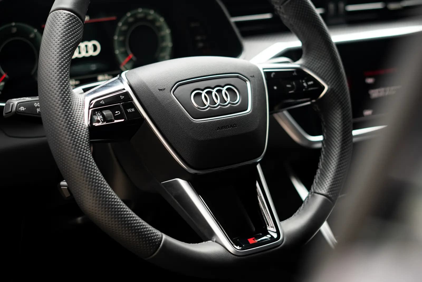 Steering wheel with the Audi badge and a red S logo, the instrument cluster blurred behind.