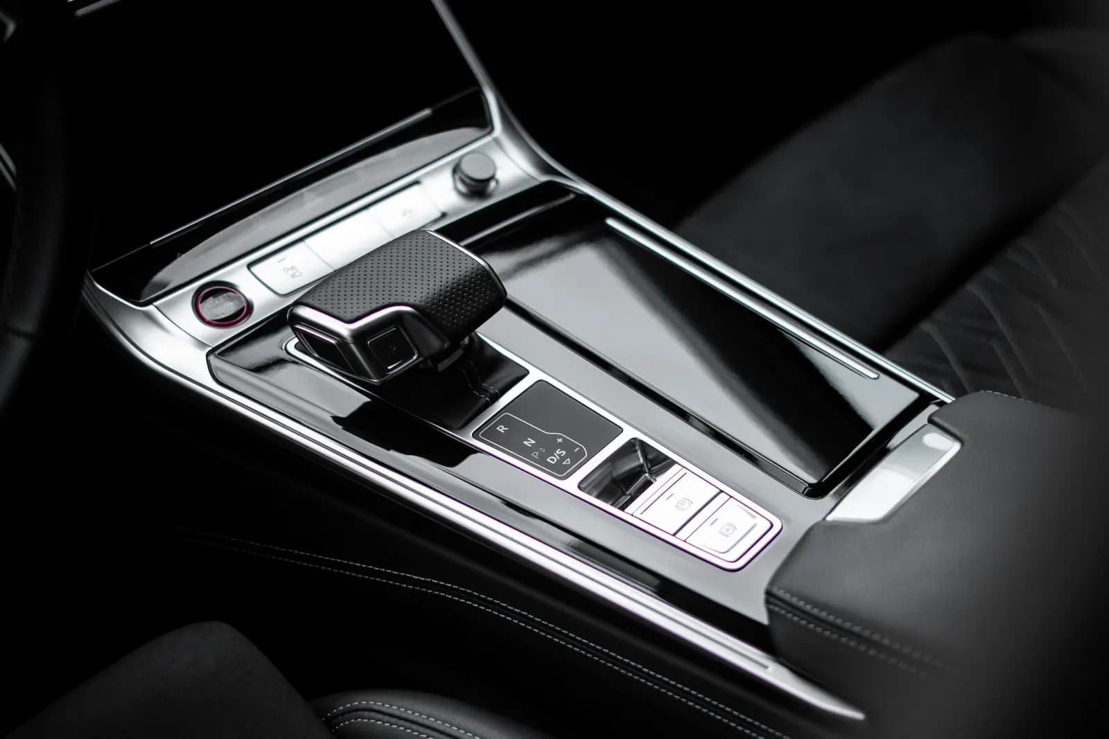 Centre console with the gear lever, drive-mode buttons and a black leather seat with white stitching.