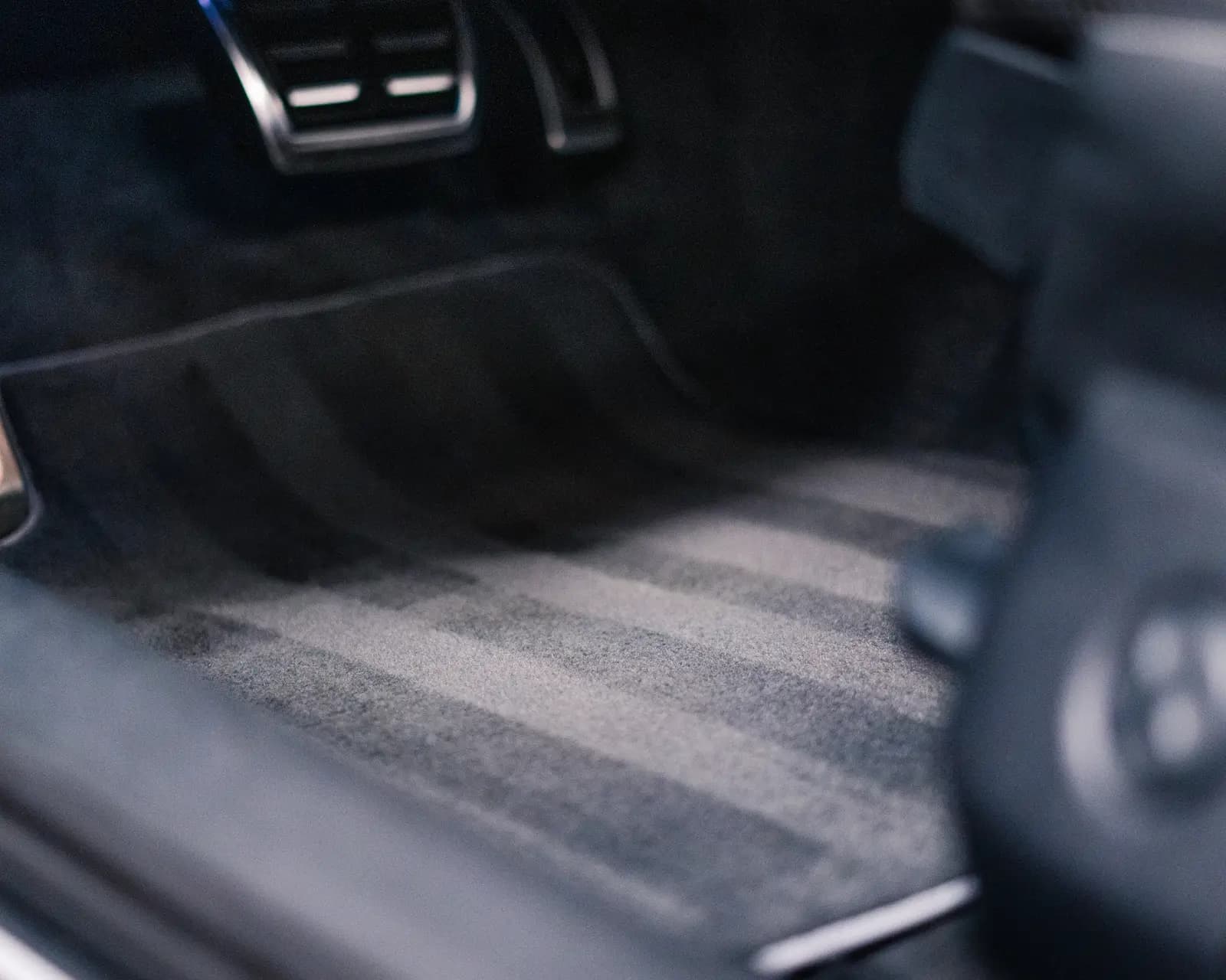 Blurred detail of a striped floor mat and sports pedals in the footwell.