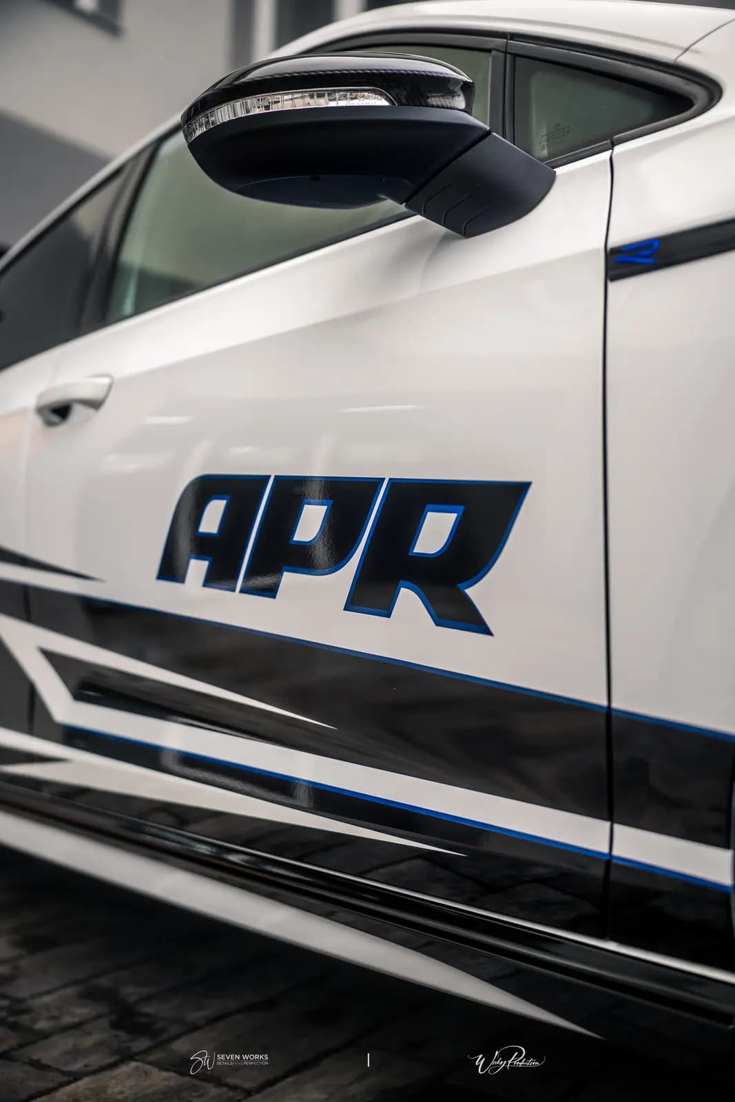 Door with large APR lettering, a carbon mirror cap and a small blue badge on the pillar of a white car.