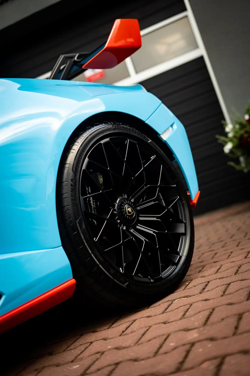 Front wheel of a light blue car with a black rim, a Bridgestone tyre and the Lamborghini badge on the centre cap.