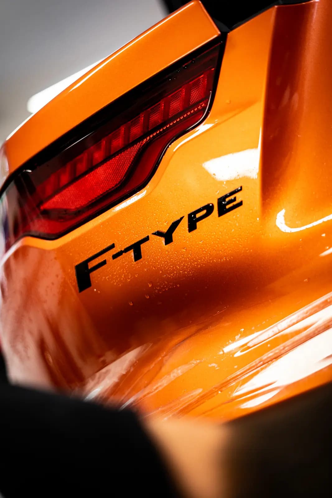 Tail light and “F-TYPE” lettering on an orange car, water droplets on the paint.