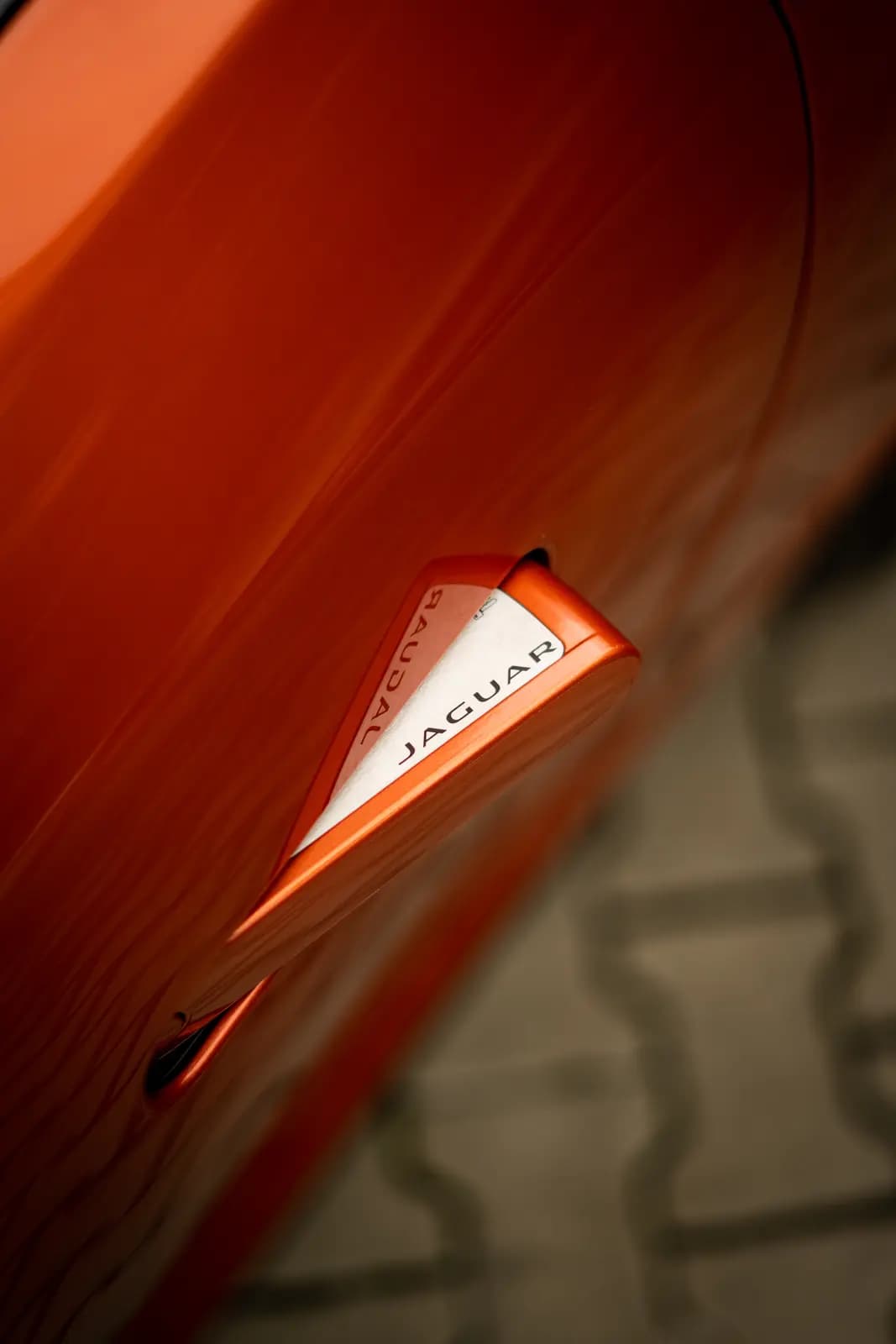Door handle with “JAGUAR” lettering on an orange car, paving blurred behind.