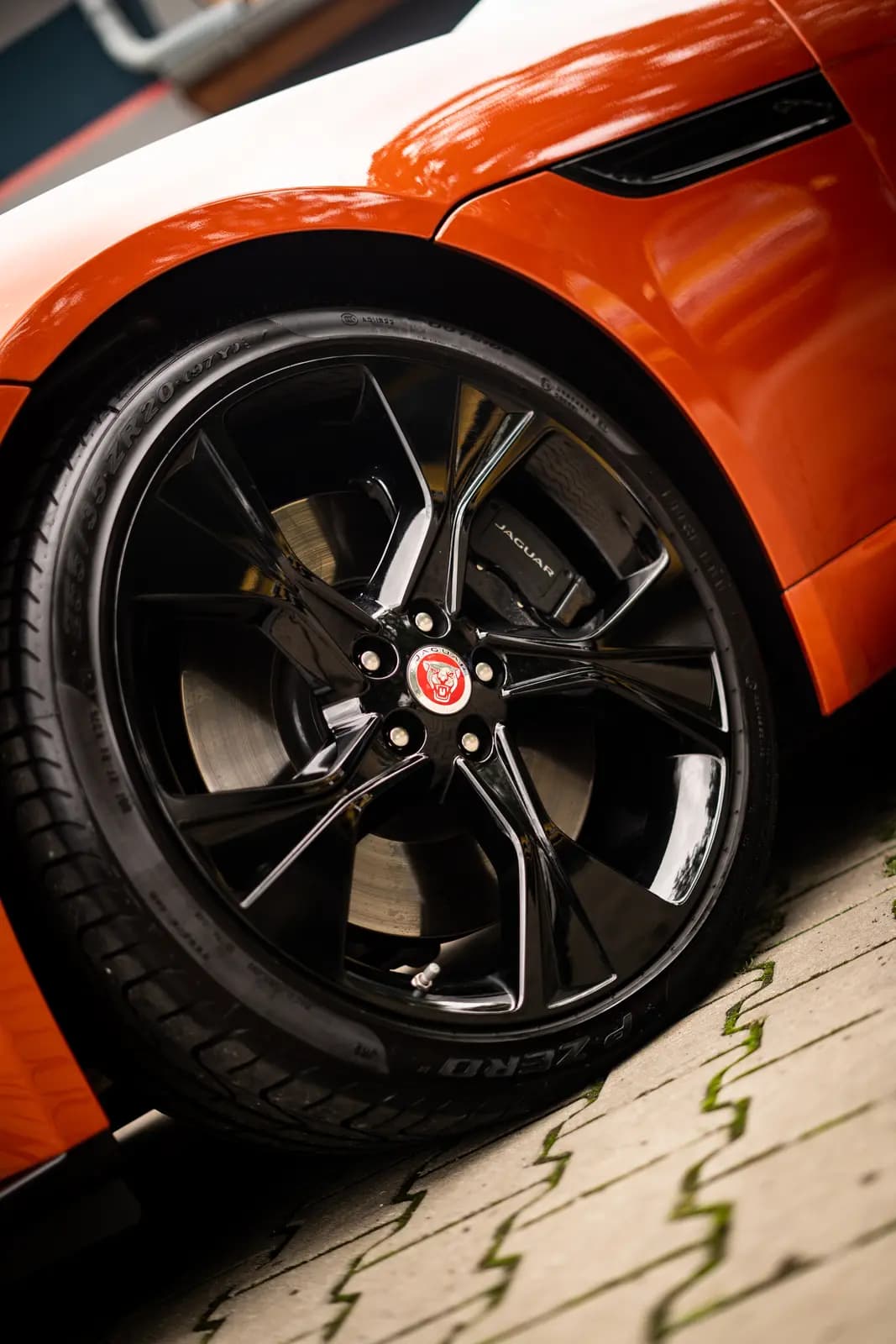 Front wheel of an orange car with a black rim, a Pirelli P Zero tyre and the Jaguar badge on both the centre cap and the caliper.