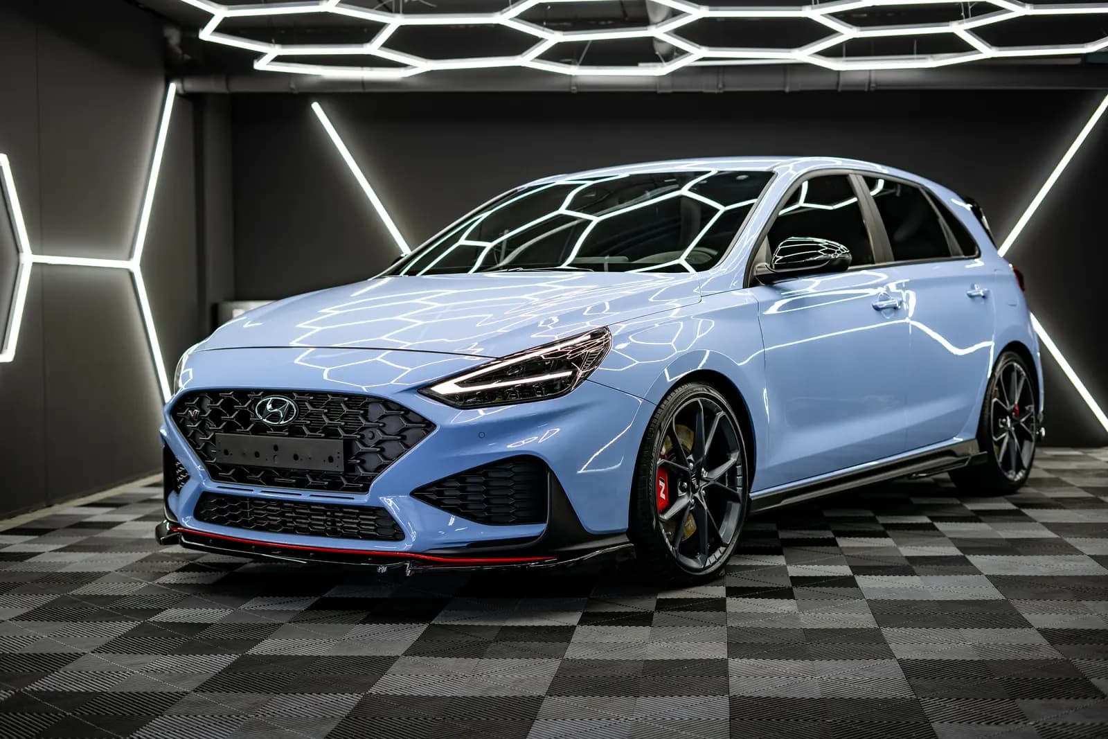 Light blue hatchback from the front in a photo studio with a suspended honeycomb light frame and a chequered floor.