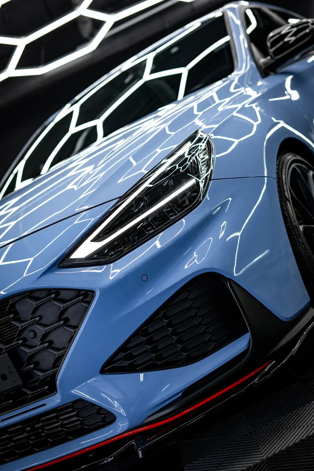 Headlight and wing of a light blue car with the honeycomb light frame mirrored in the paint.