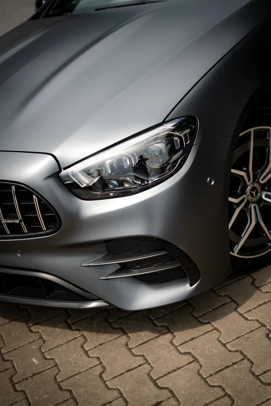 Headlight and grille with AMG lettering on a matte grey Mercedes.