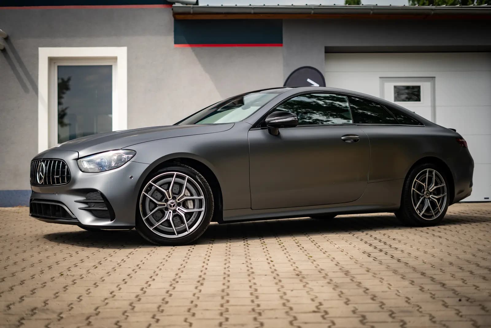 Side view of a matte grey Mercedes-AMG coupe parked in front of a building with garage doors.