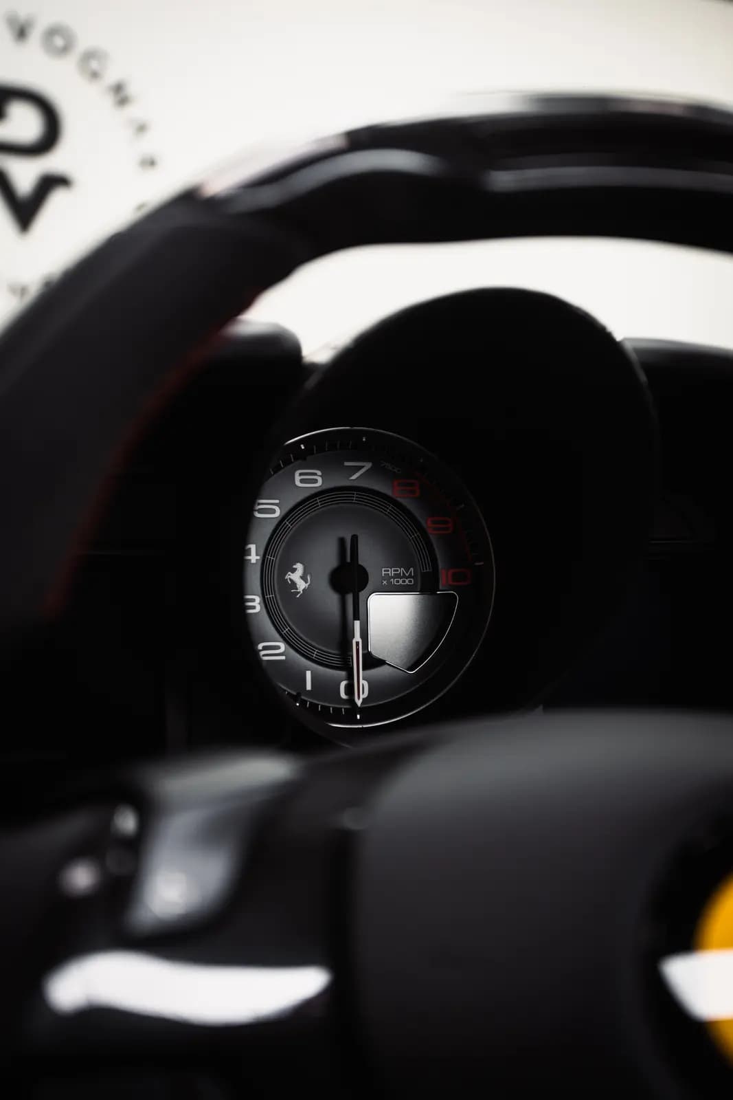 Rev counter with the Ferrari logo and a steering wheel with red stitching.