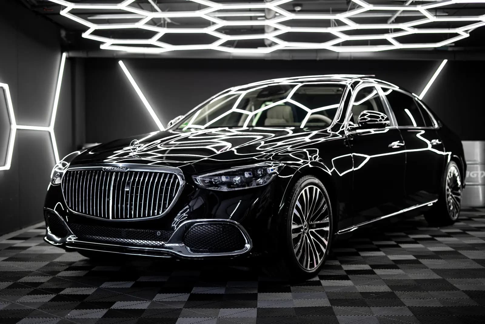 Black Mercedes-Maybach standing front-on in a studio with hexagonal LED lighting and a chequered floor, MAYBACH legible on the grille.
