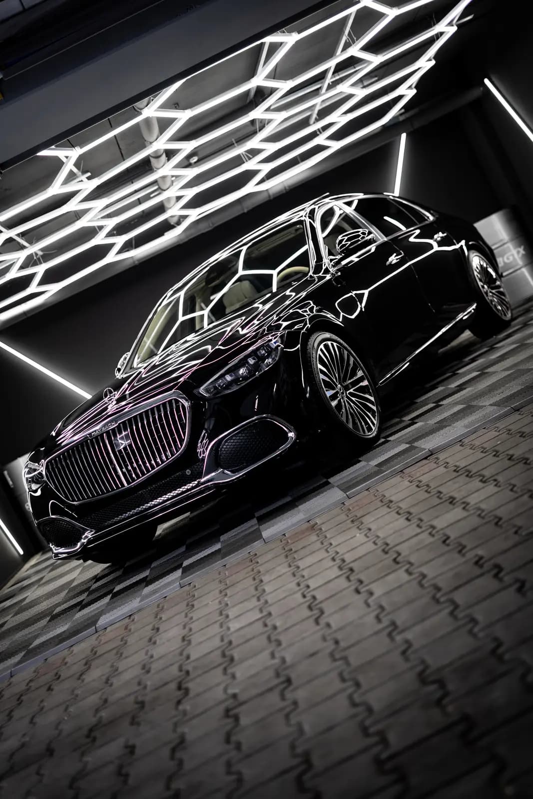 Black Mercedes-Maybach from a low front angle in the same studio, MAYBACH legible on the grille, a metal drum behind.