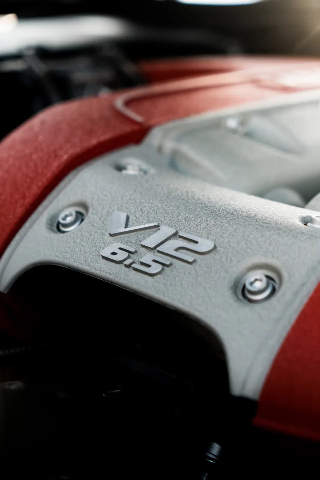 Aluminium engine cover reading V12 6.5 on a red ground, bolts around it.