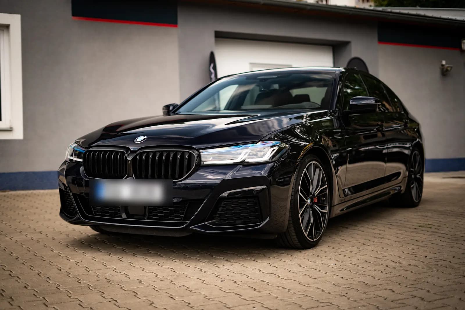 Černé BMW řady 5 zepředu, zaparkované na dlažbě před budovou.