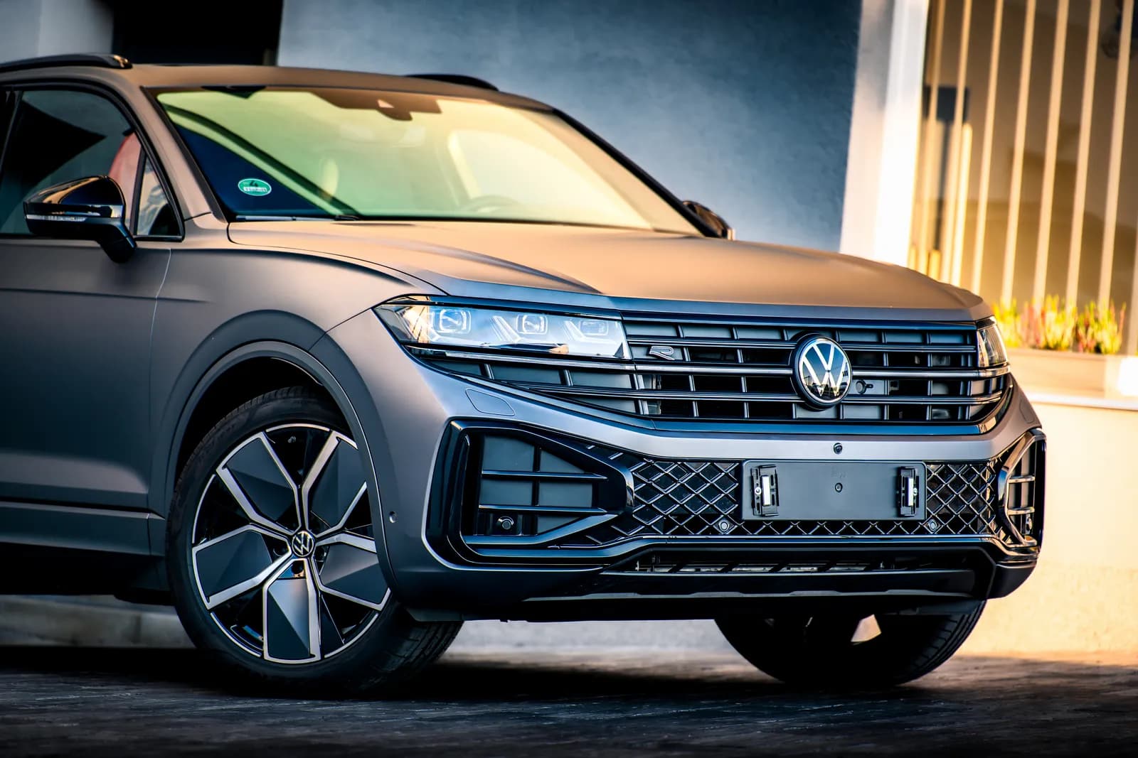 Přední část a kolo Volkswagenu Touareg v matné šedé fólii, záběr z nízkého úhlu před budovou provozovny.