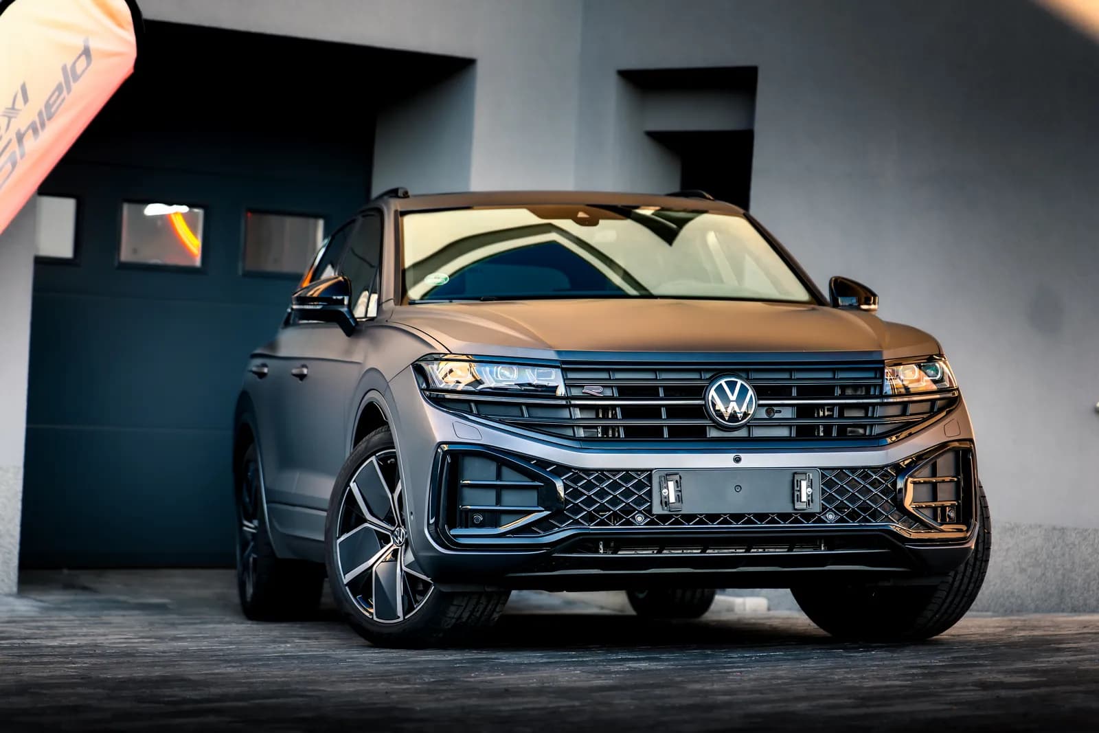 Volkswagen Touareg v matné šedé fólii přímo zepředu, před tmavými garážovými vraty provozovny.