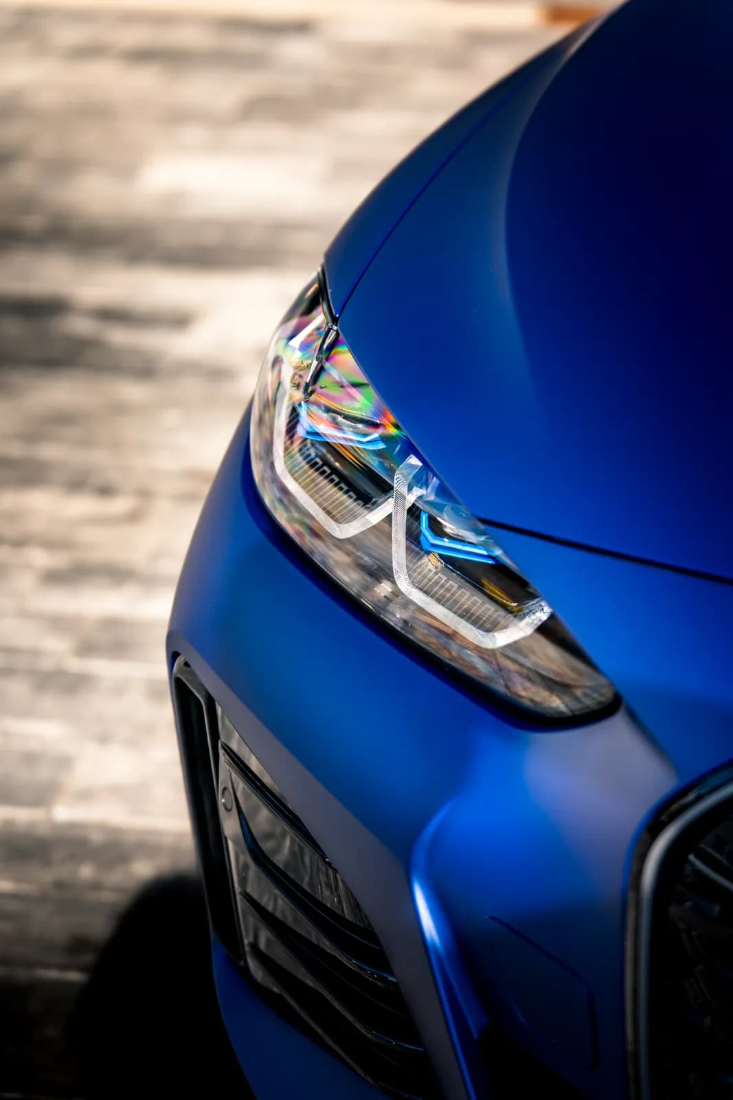 Detail předního světlometu a kapoty matně modrého BMW i4, matný povrch v ostrém světle.