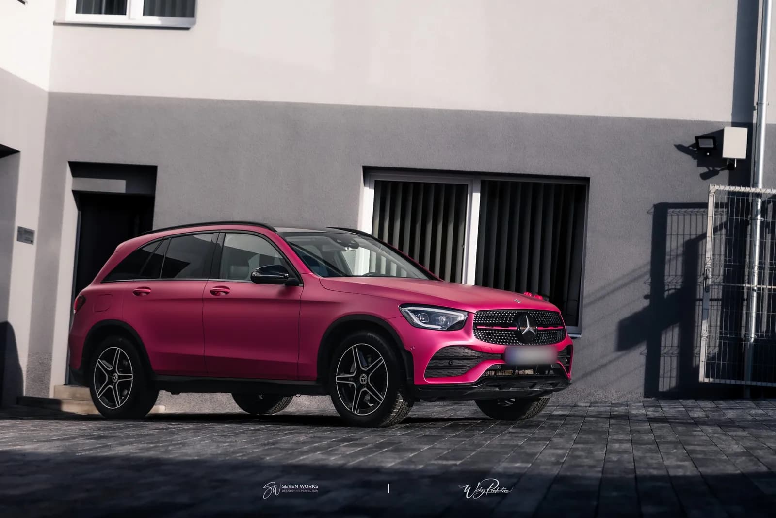 Růžově polepené SUV Mercedes-Benz z boku před šedou fasádou provozovny.
