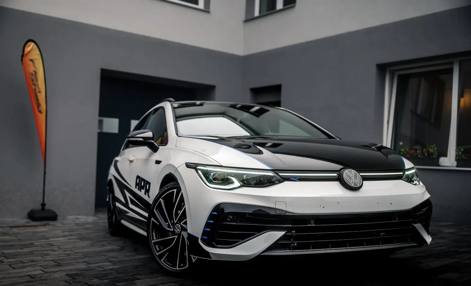 Přední tříčtvrteční záběr vozu VW s dvoubarevným designovým polepem a vlajkou v pozadí.