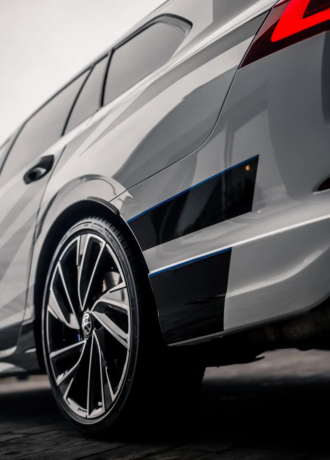Detail zadního boku světle šedého vozu s černým designovým polepem lemovaným modrou linkou.