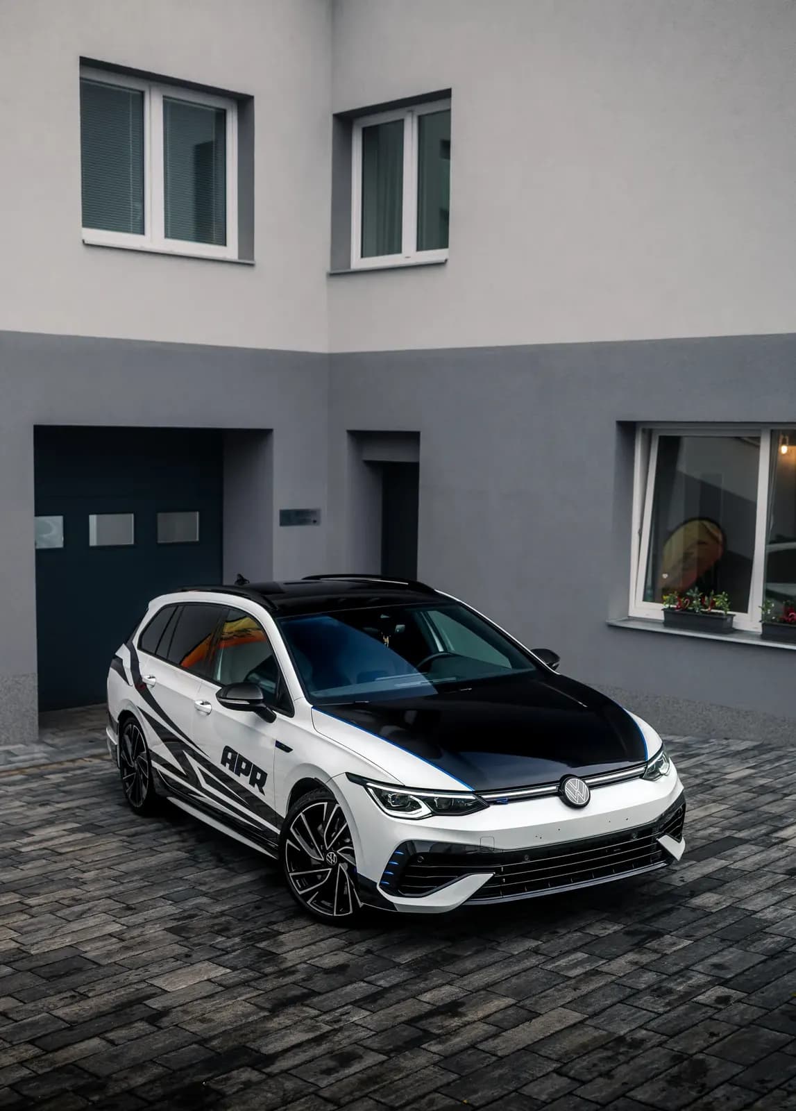 Přední tříčtvrteční záběr vozu VW s designovým polepem na dvorku před domem.