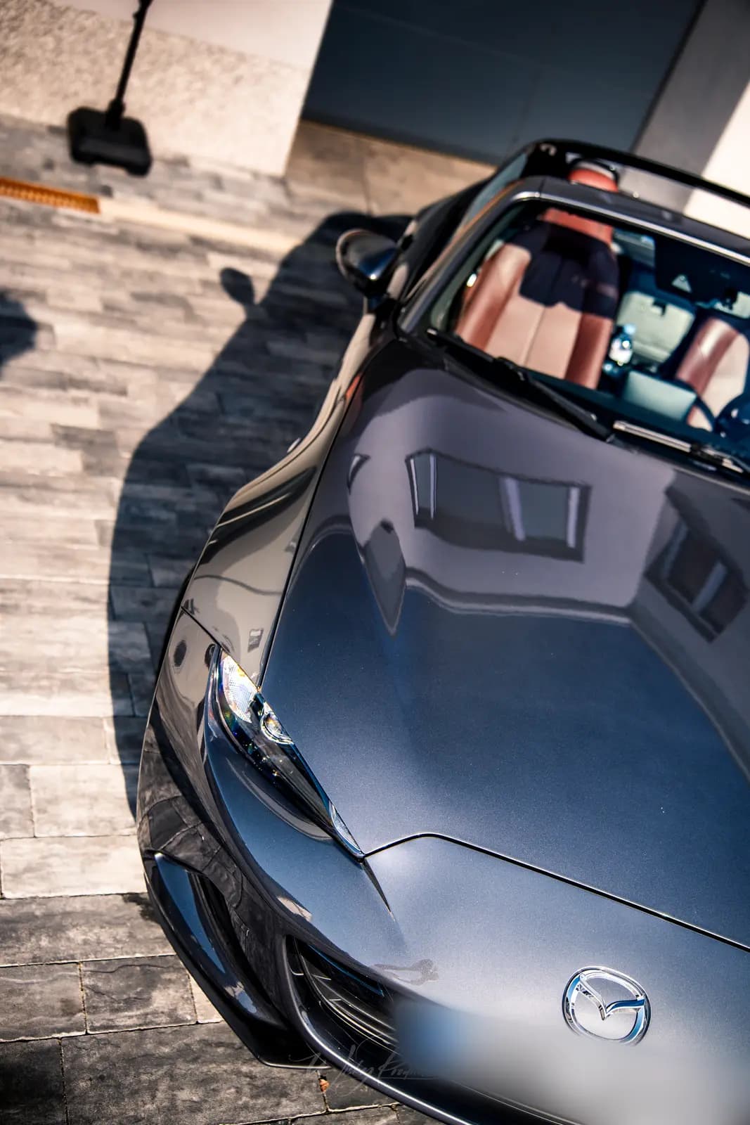 A top-down view of the Mazda MX-5 bonnet, with tan leather seats visible behind the glass.
