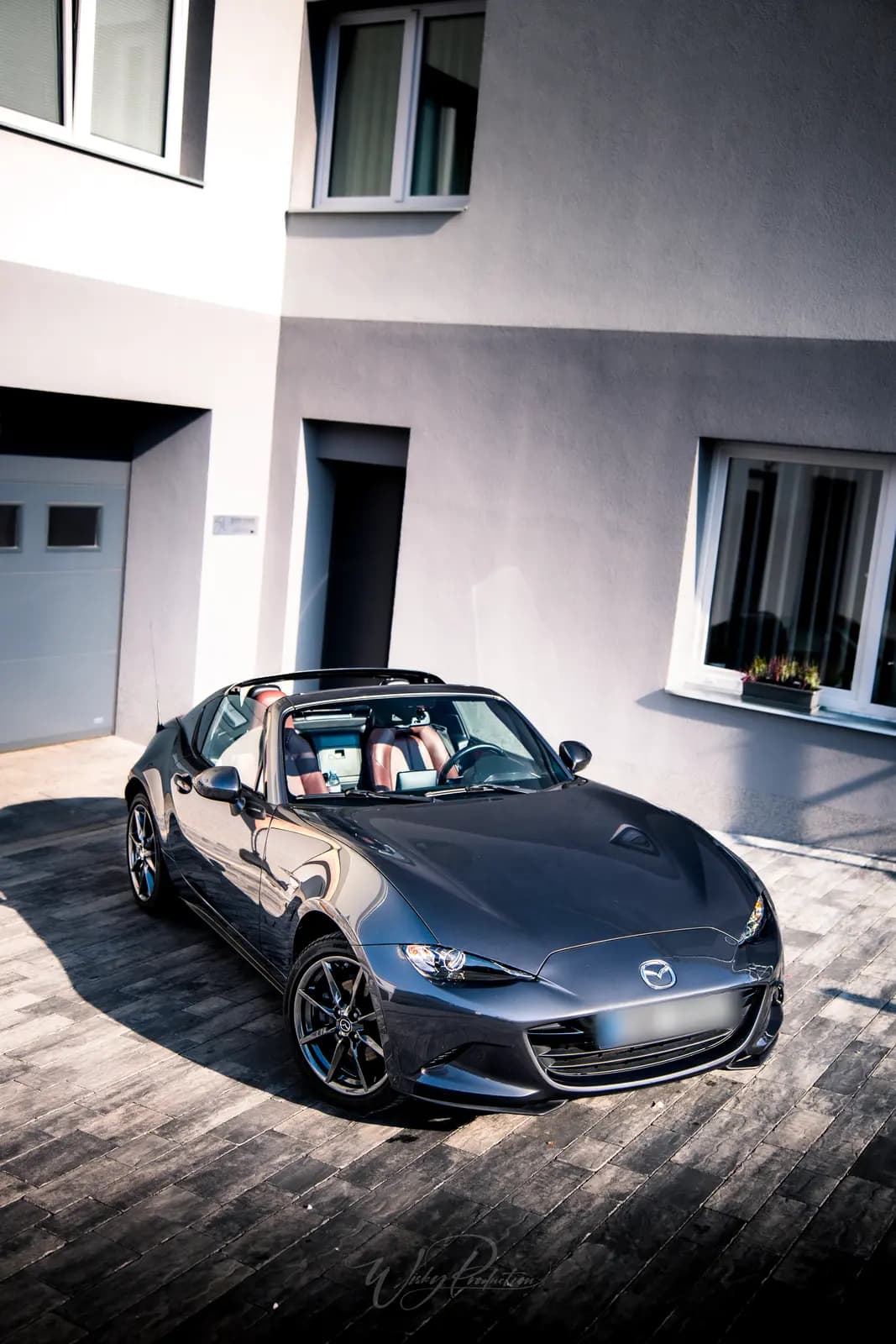 A Mazda MX-5 RF seen from the front on paving outside the studio, the sun casting the car’s shadow.