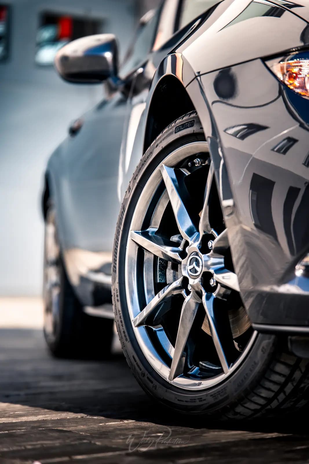 Close-up of a Mazda MX-5 front wheel with polished spokes and the wing above it.