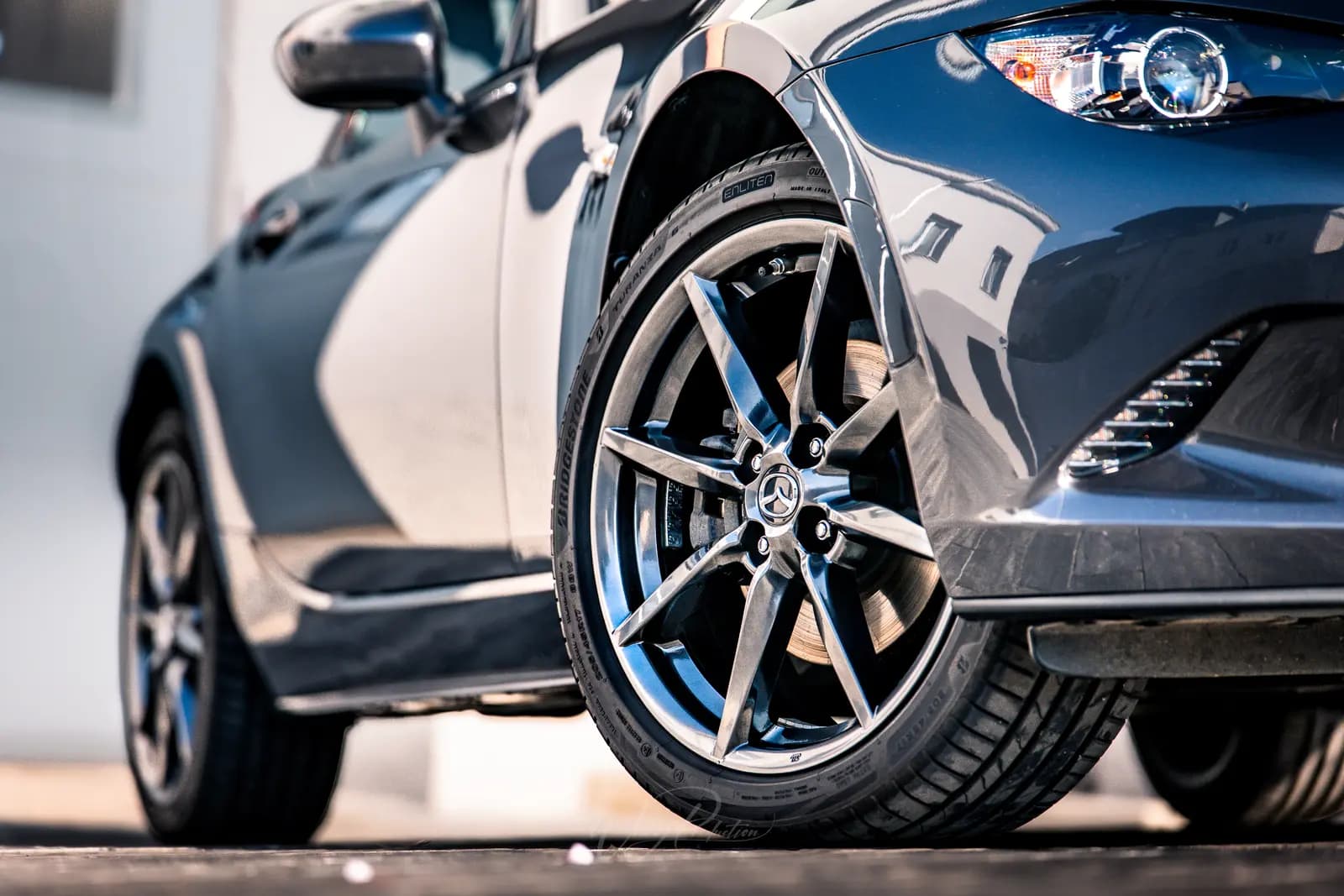 Detail předního kola a světlometu Mazdy MX-5, karoserie se zrcadlí v laku.