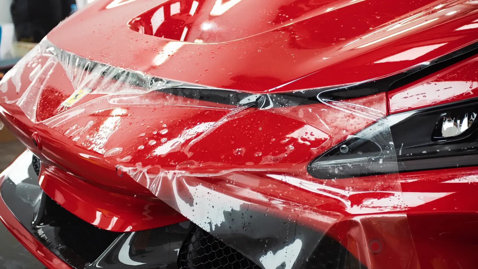 Detail mokré fólie nalepené na přední masce a světlometu červeného Ferrari.