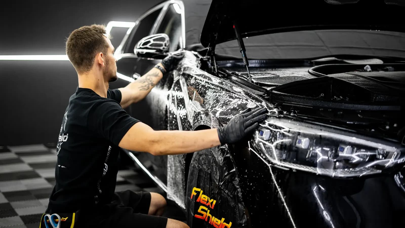 Technik ve studiu se značkou Flexi Shield lepí fólii na přední blatník černého vozu.