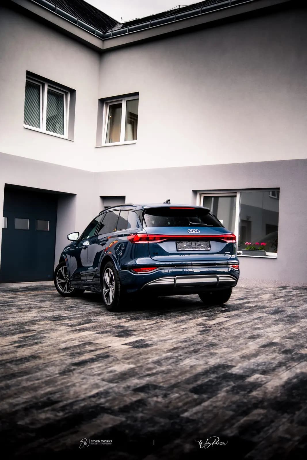 Zadní pohled na tmavě modré Audi Q6 e-tron před budovou provozovny.