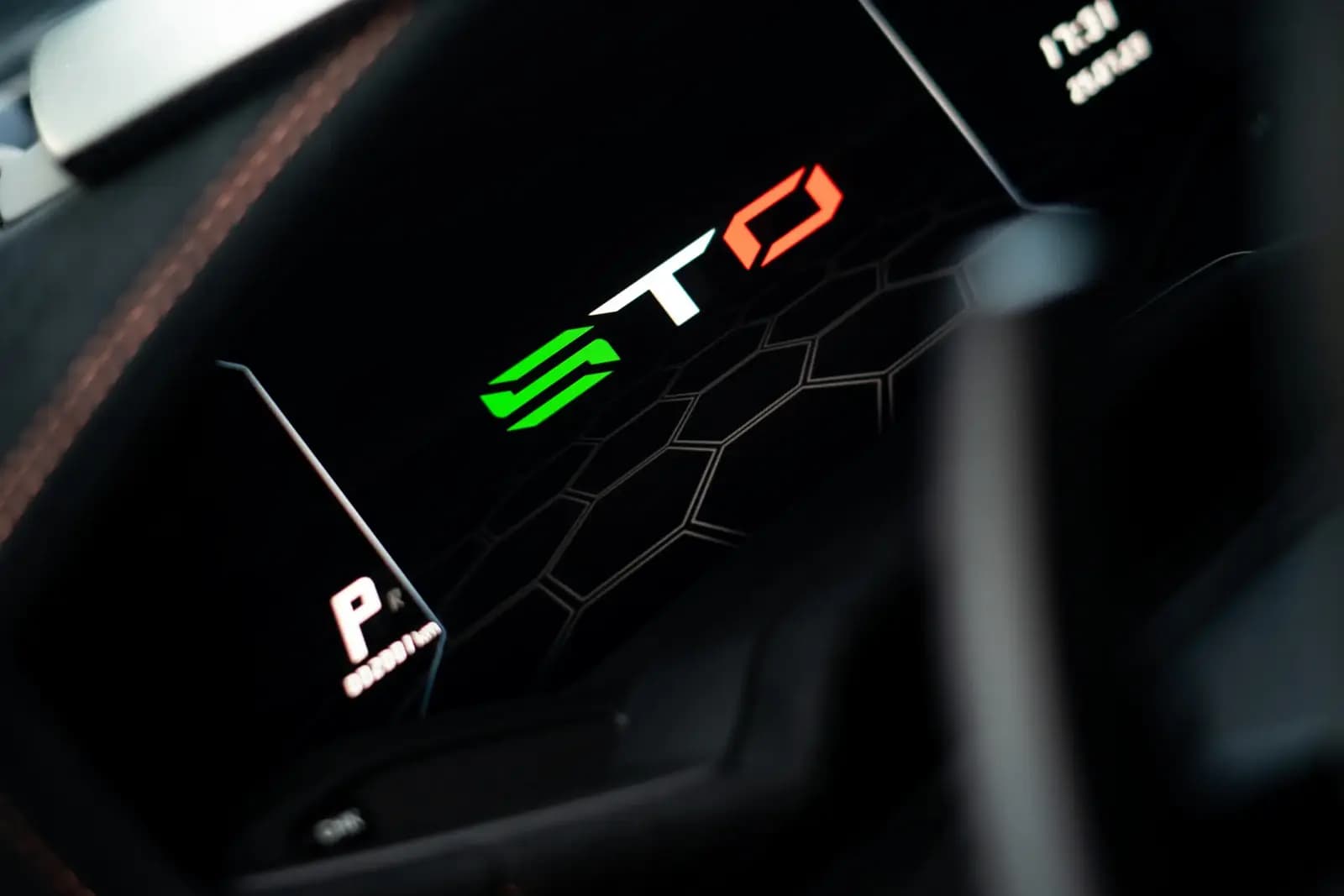 Detail podsvíceného přístrojového displeje sportovního vozu s logem STO.