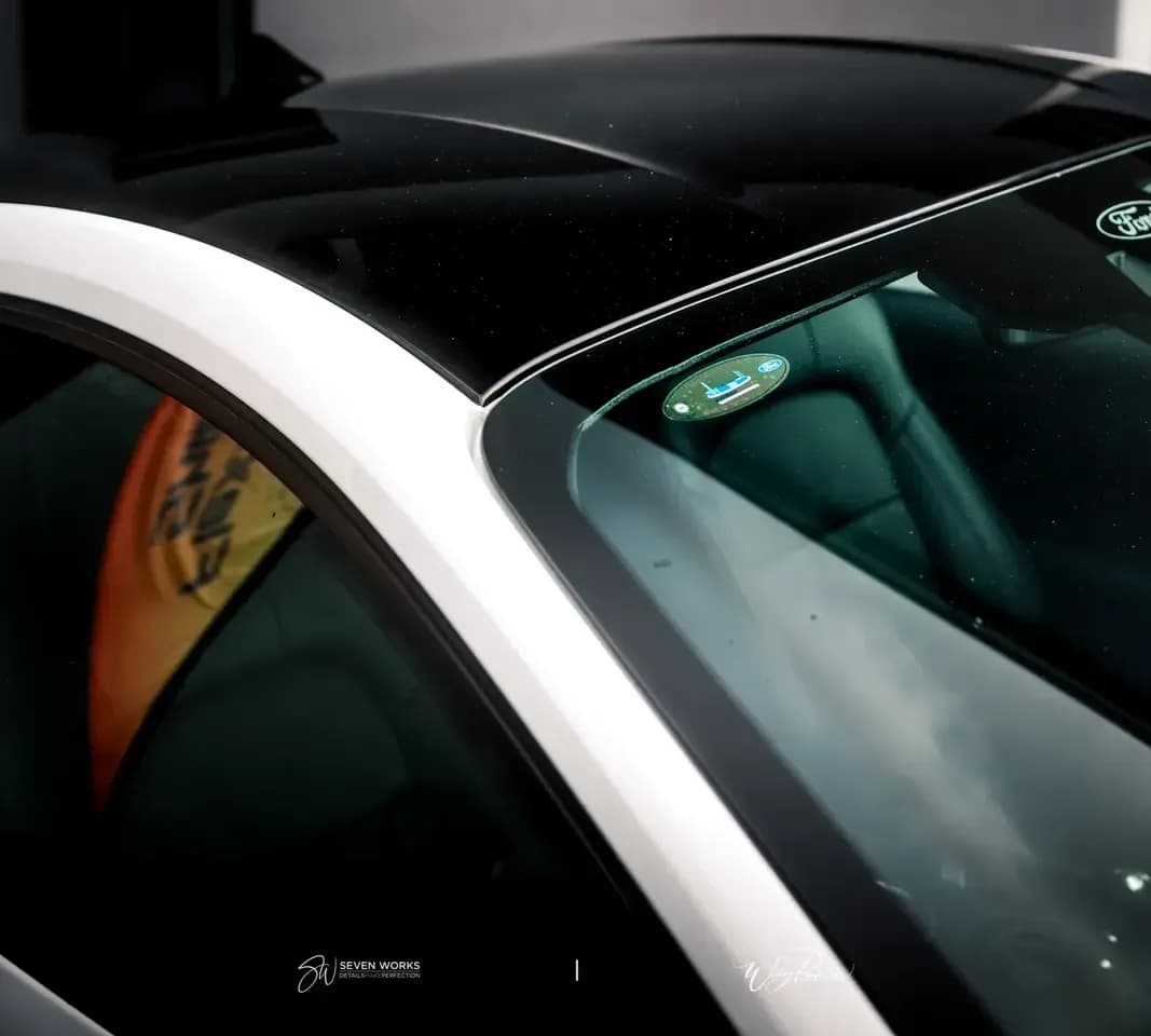 Close-up of a car's roof and windscreen with the orange flag reflected in tinted glass.