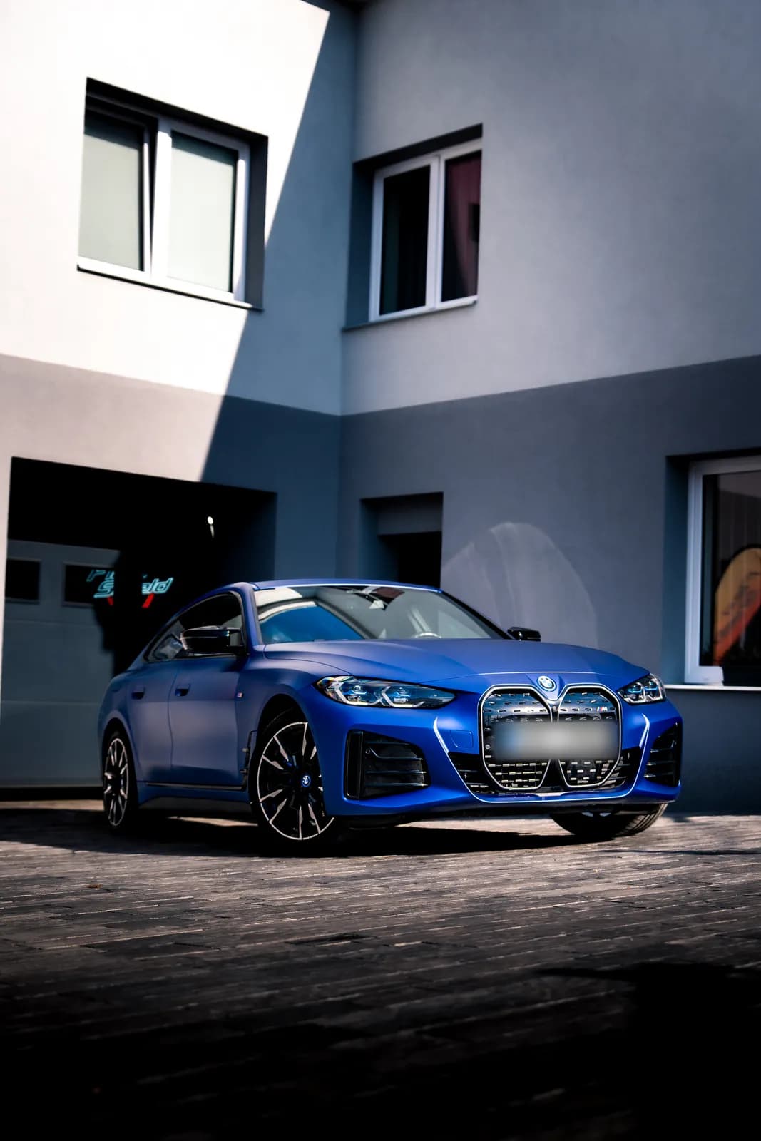 A matte blue BMW i4 from the front outside the studio building, the whole car in view.