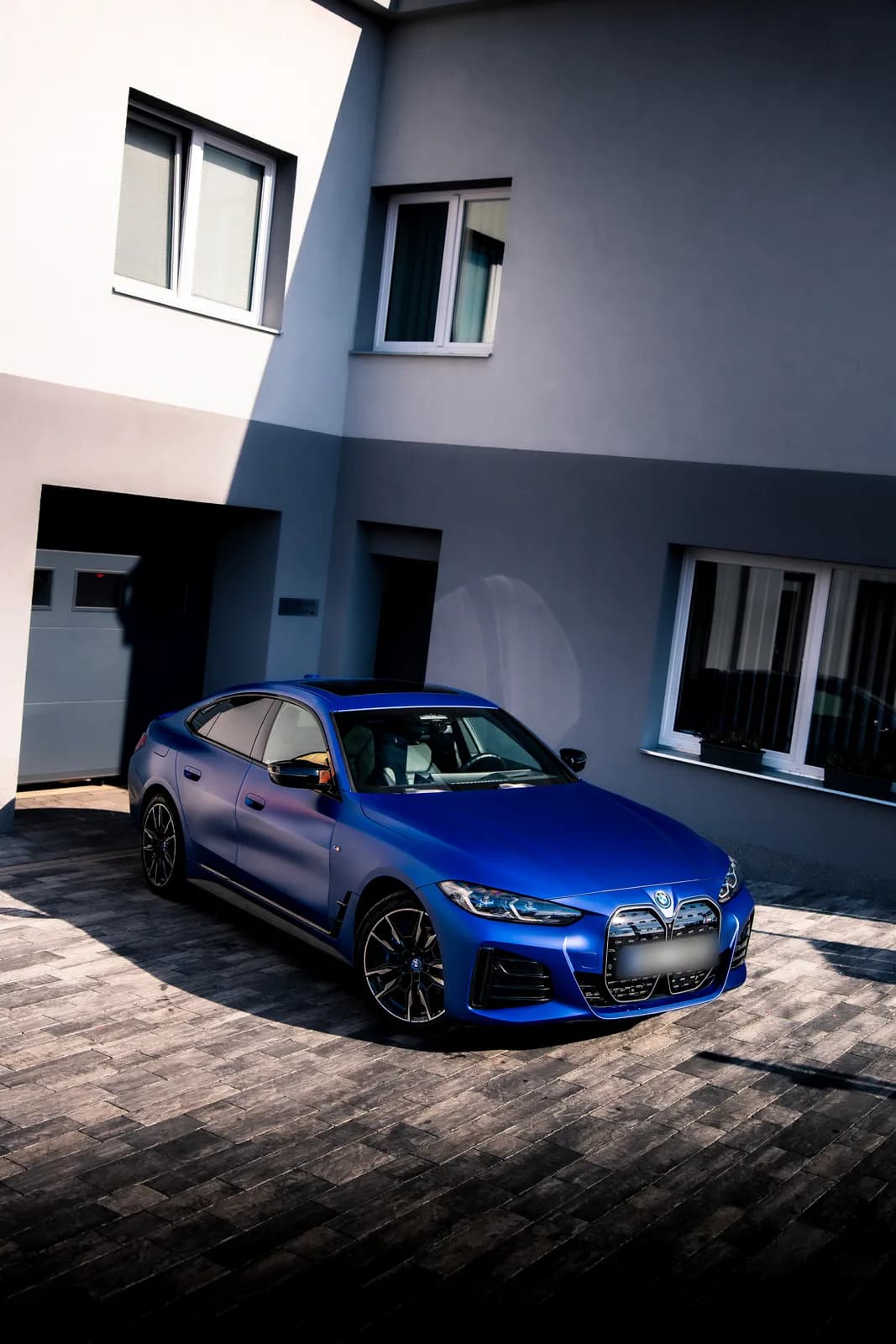A matte blue BMW i4 from the front quarter on the paved yard outside the studio.
