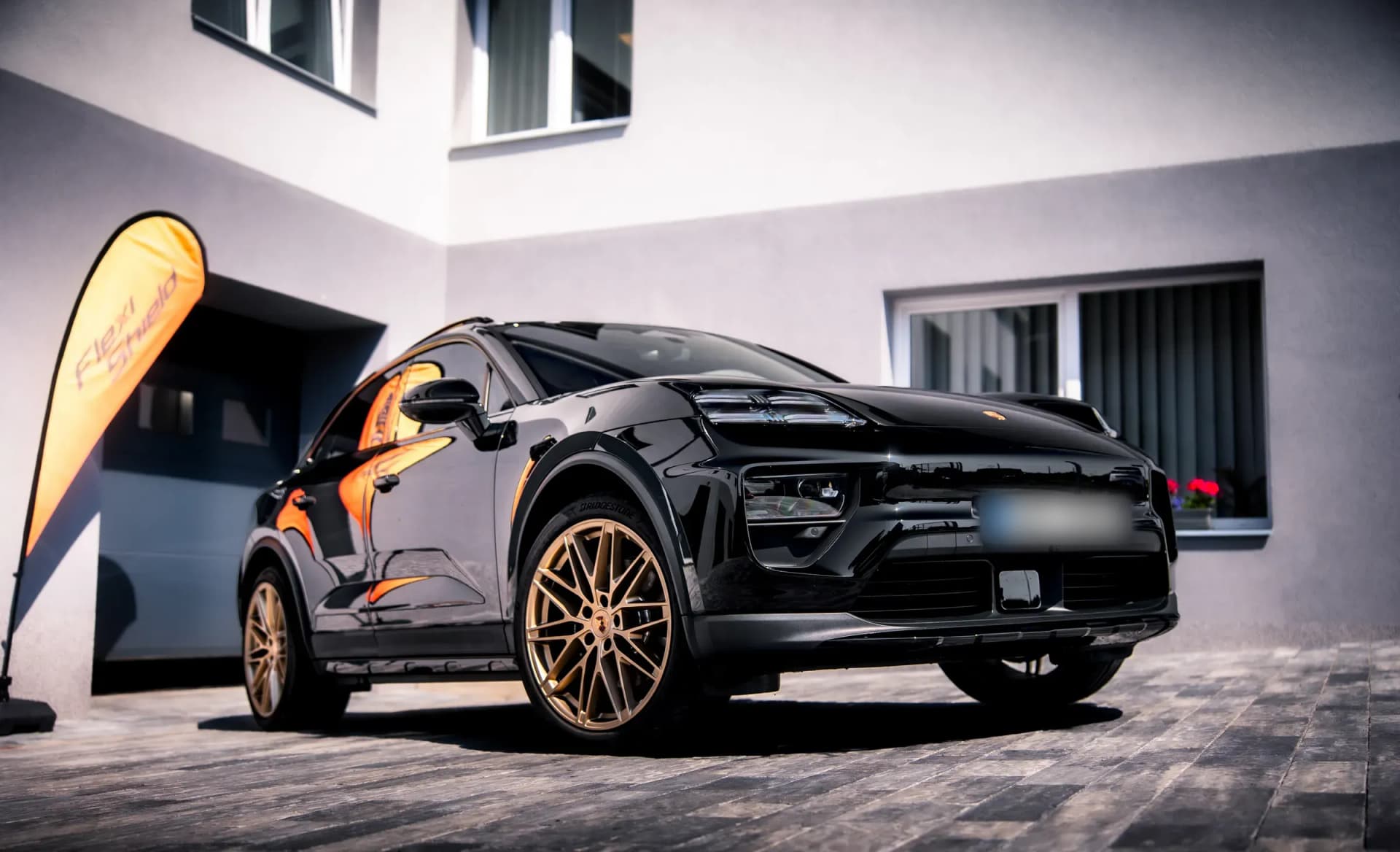 A black Porsche viewed from the front at an angle, on the driveway outside the workshop.