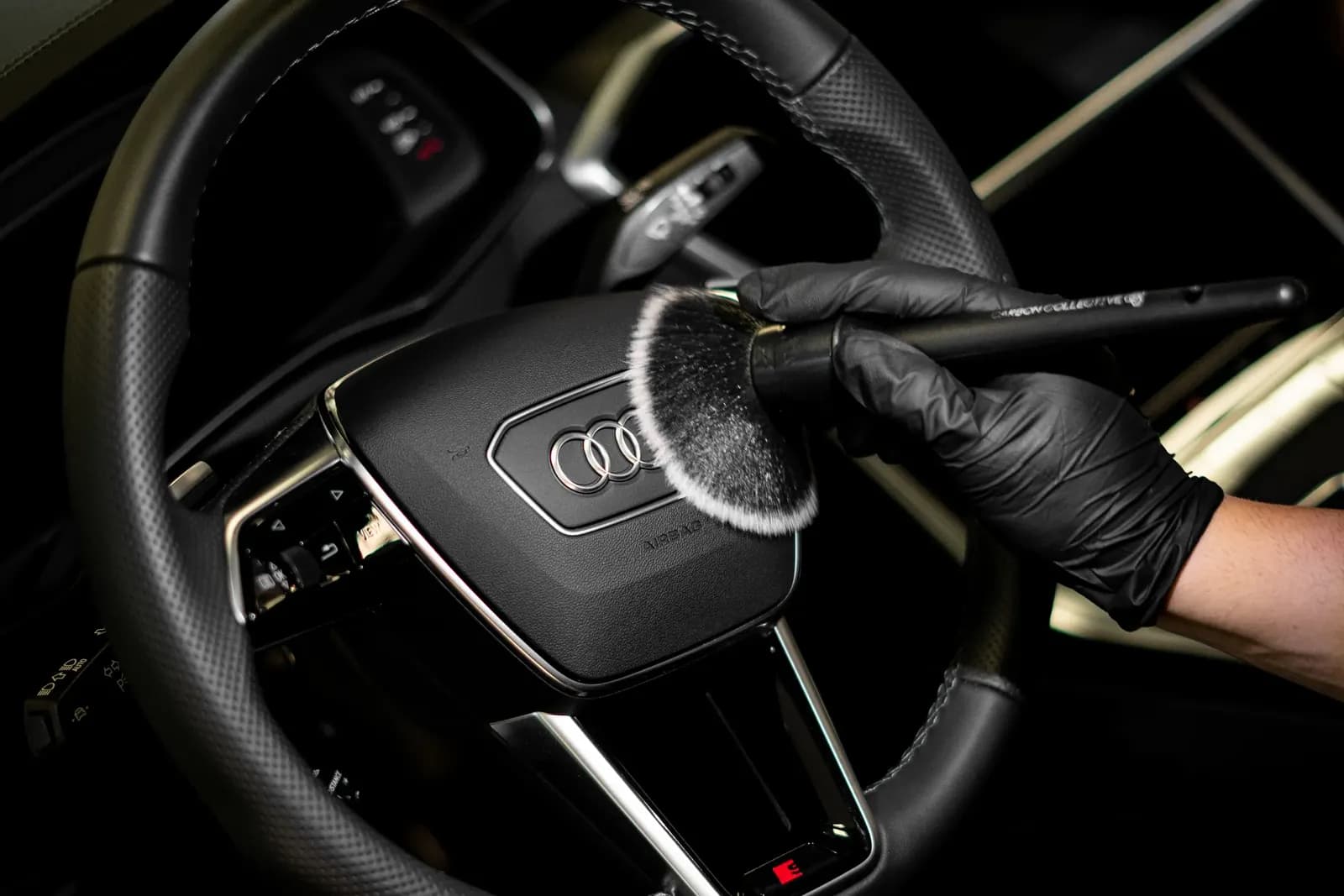 Ruka v rukavici čistí detailingovým štětcem znak Audi na volantu.