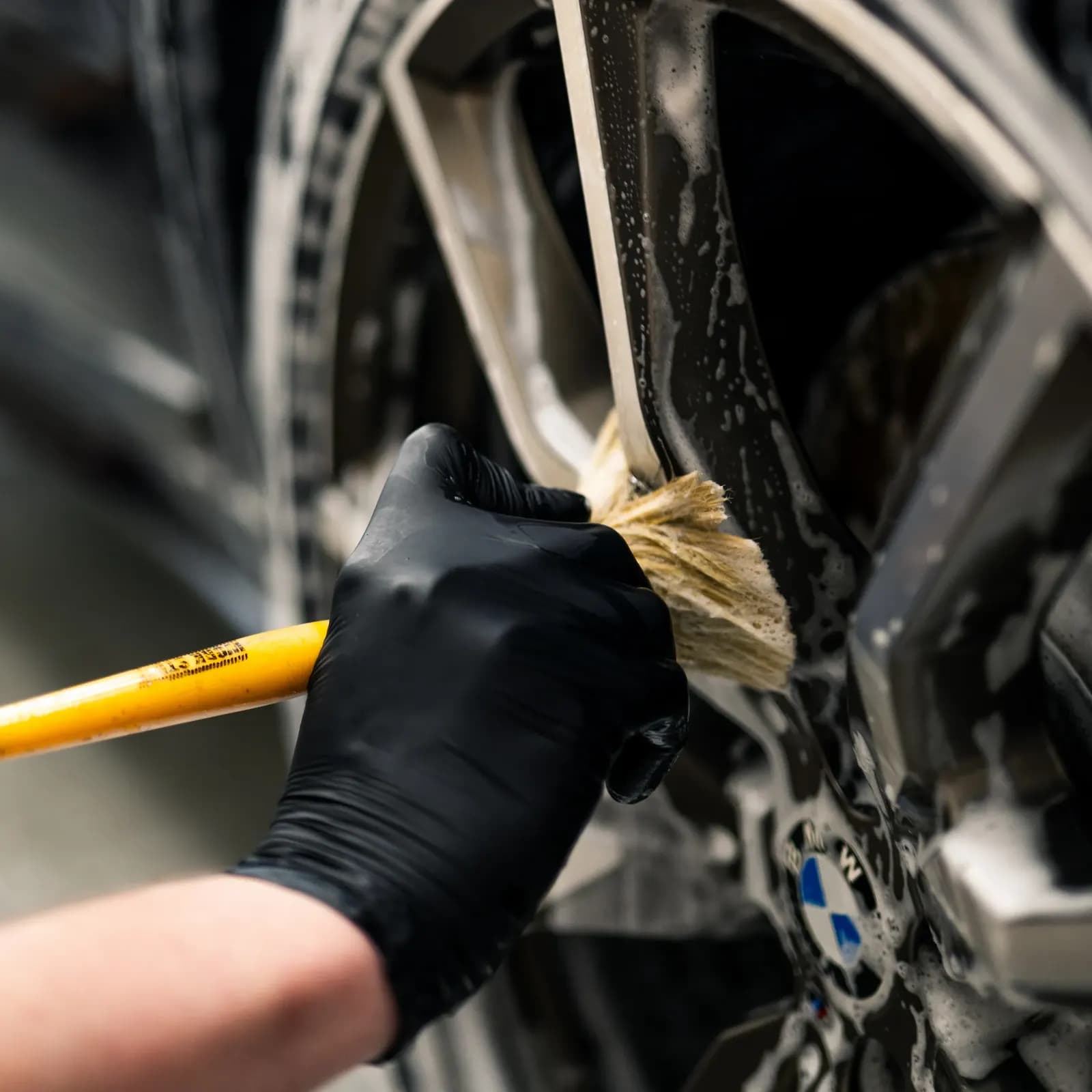 Detailní mytí disku kola BMW kartáčem, viditelné logo BMW.